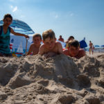Dzieci leżące na plaży pomiędzy dwoma wychowawczyniami zakopanymi w piasku.